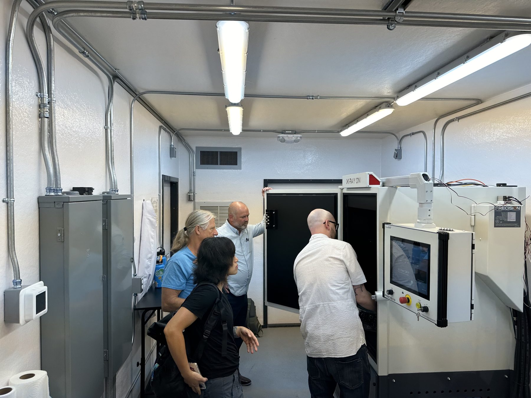 A group of people inspecting and discussing an x-ray sterilization machine used for insect sterilization in a well-organized lab environment.