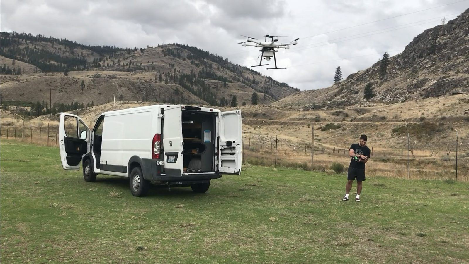 An M3 release van parked in a field with its doors open while a pilot flies a release drone overhead