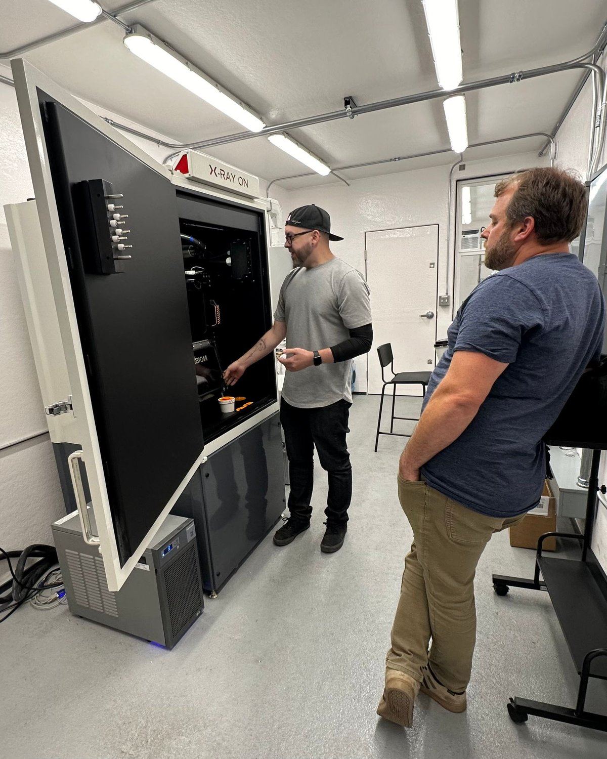 Two people beside an open X-RAD 320 X-ray irradiator with its X-RAY ON light lit